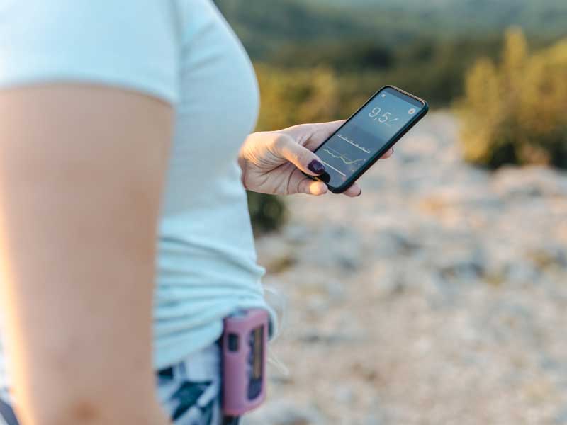 Woman with diabetes wearing an insulin pump and checking her blood glucose on a smart phone app
