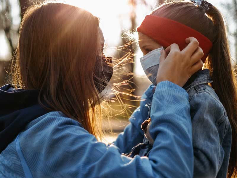 A girl with a child is standing on the road in a protective medical mask